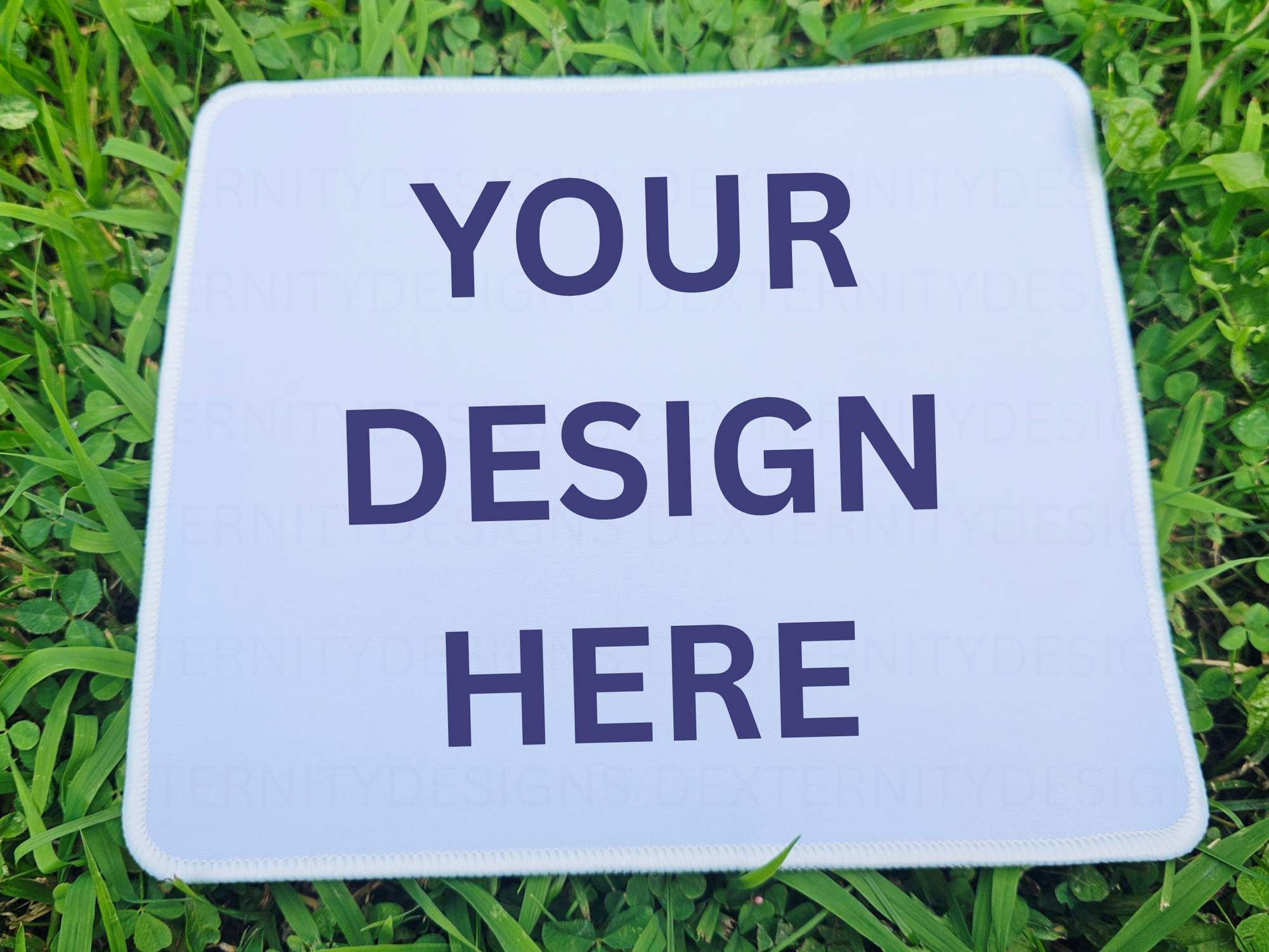 White mousepad with 'Your Design Here' text on grass