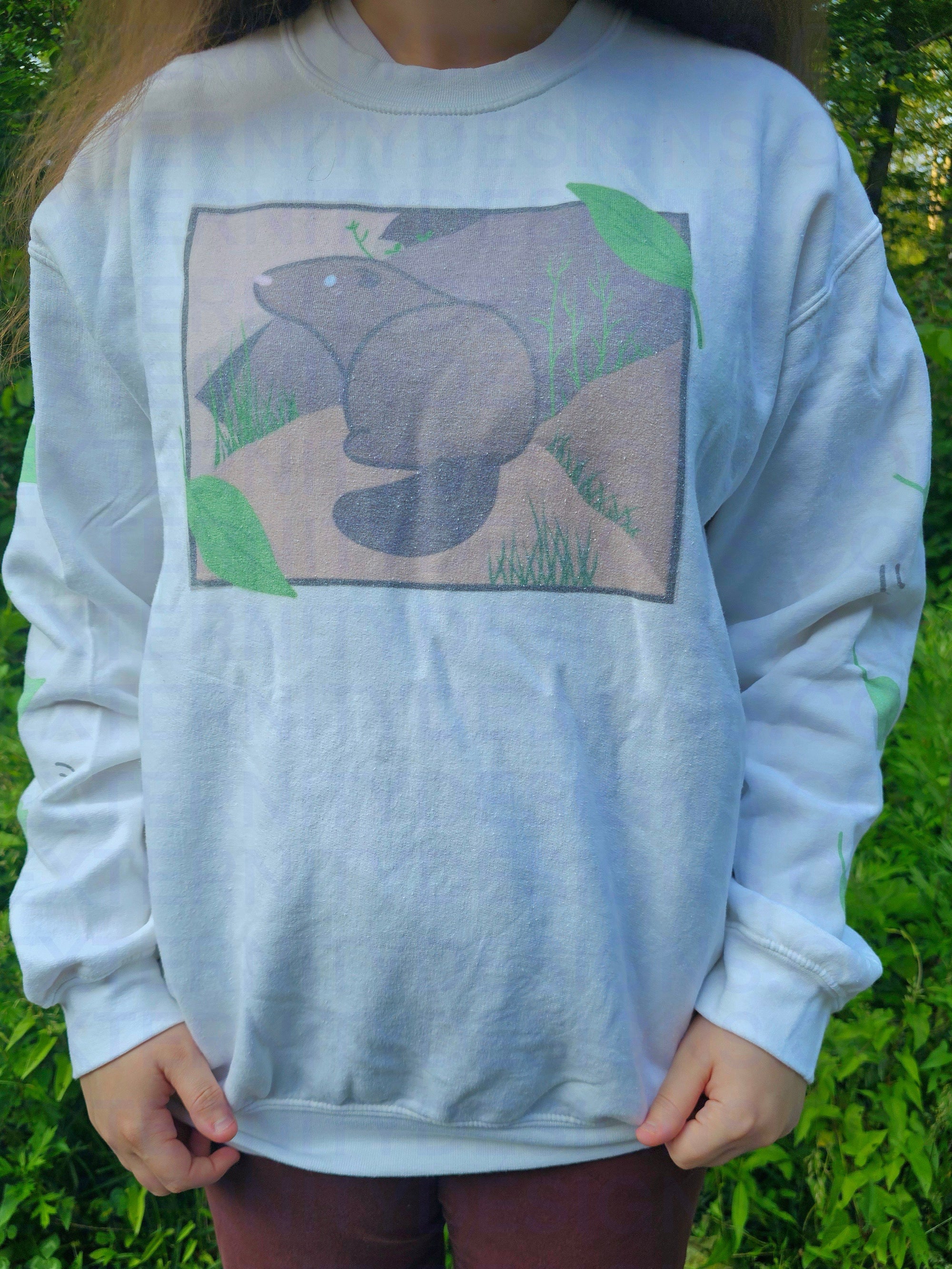 A person wearing a white sweatshirt featuring a groundhog drawing on the chest and leaves on the sleeves.