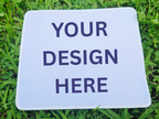 White mousepad with 'Your Design Here' text on grass