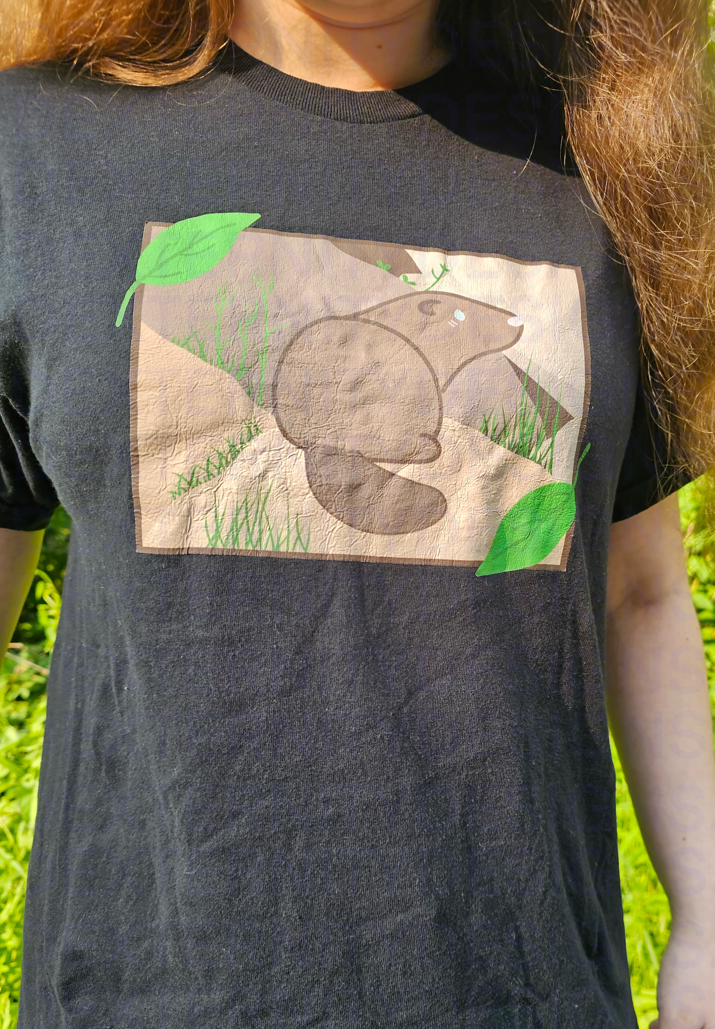 Person wearing a black t-shirt with a graphic design of a groundhog outdoors.