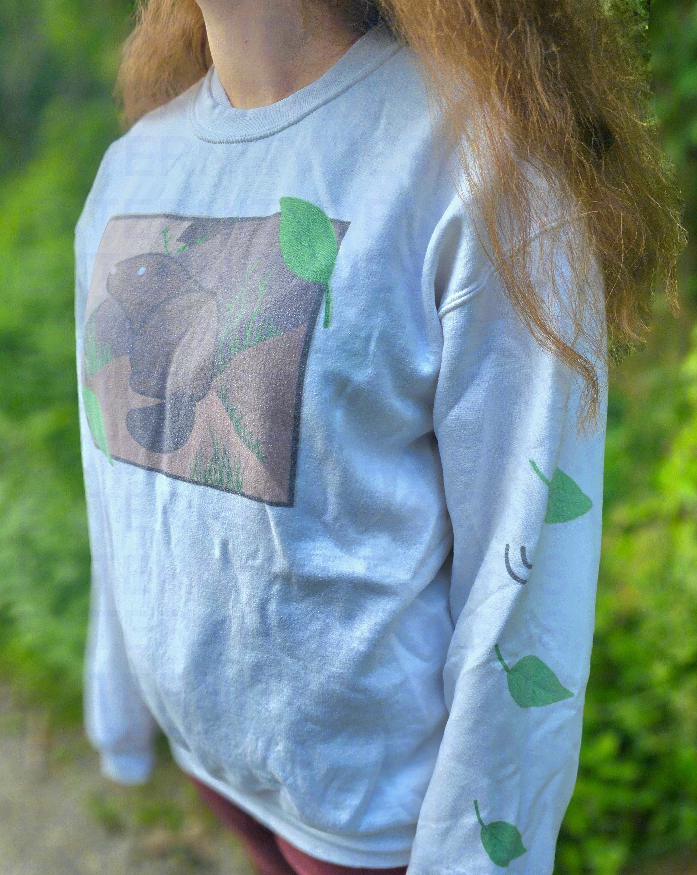 A person wearing a white sweatshirt featuring a groundhog drawing on the chest and leaves on the sleeves.