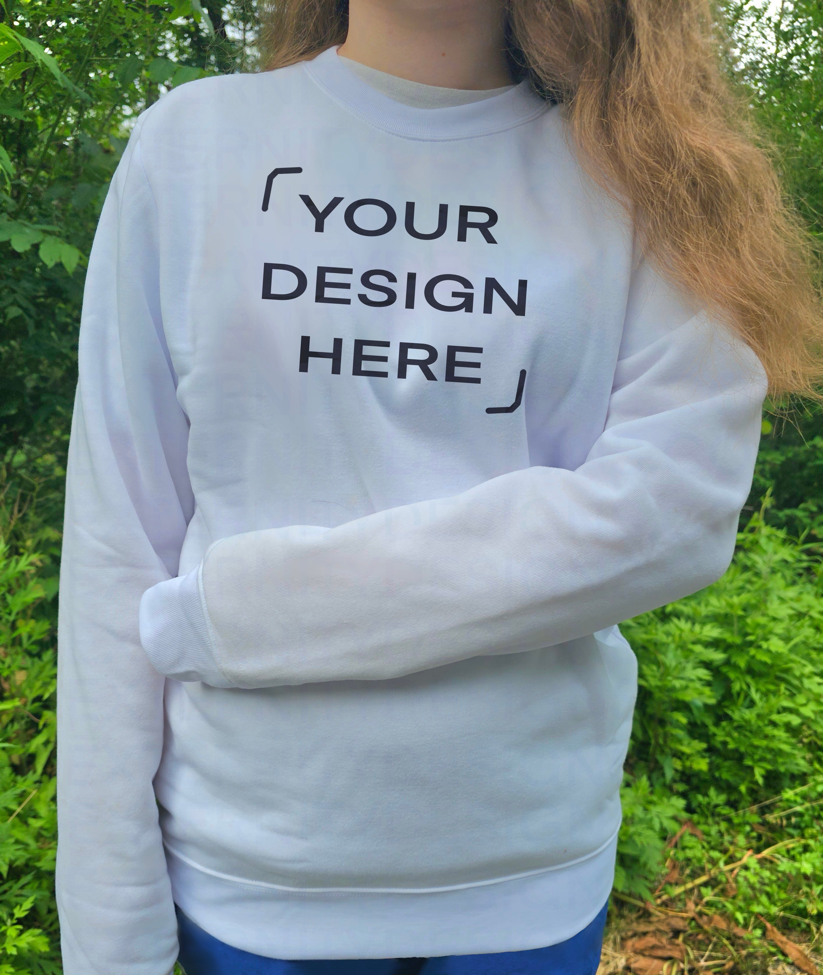 A person with their arm across their stomach wearing a white sweatshirt with "YOUR DESIGN HERE" outdoors.