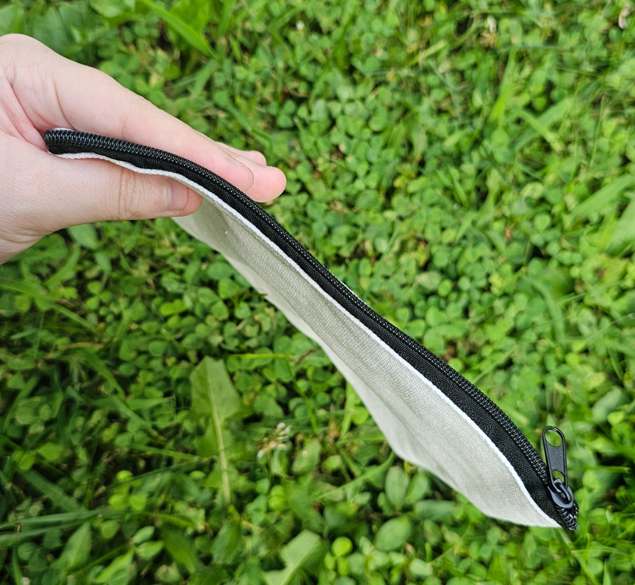 White pouch with a black zipper held by a hand on grass