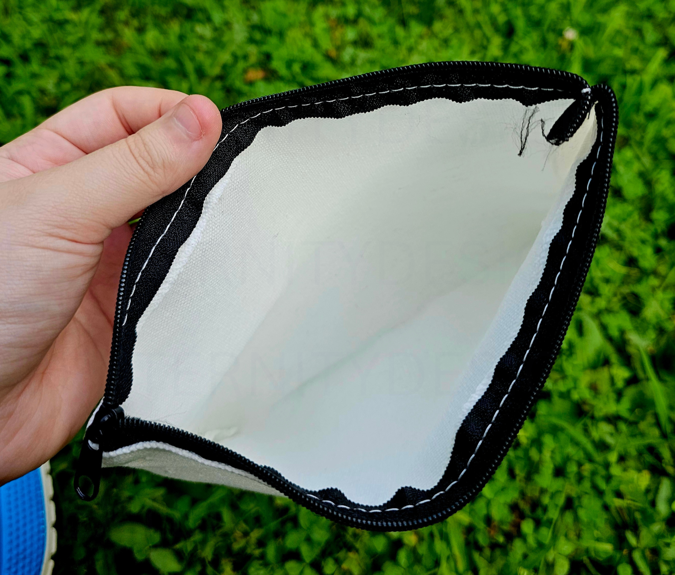 Hand holding a white pouch with black trim against a grass background