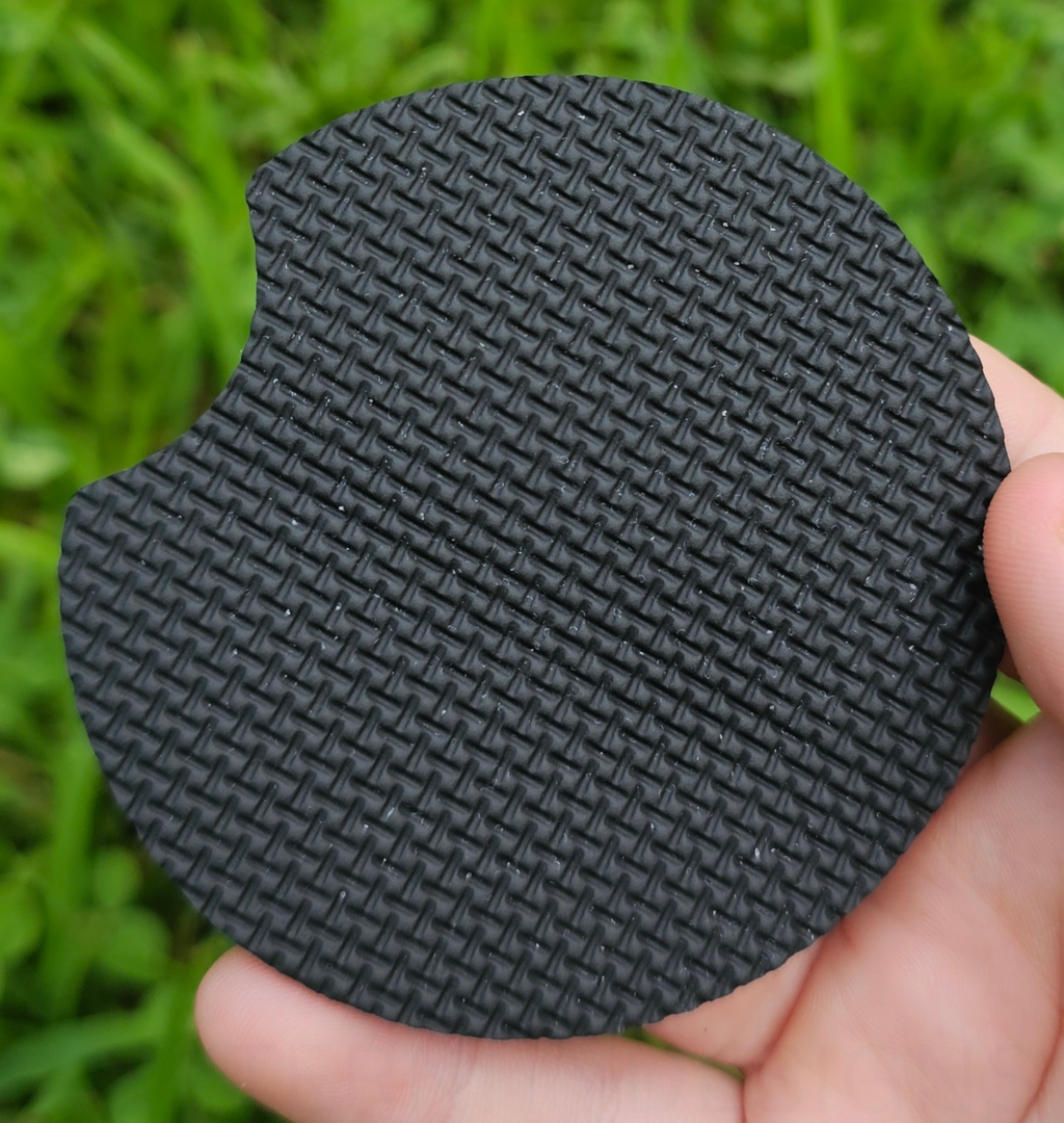 Hand holding a circular coaster designed for car cup holders upside down.